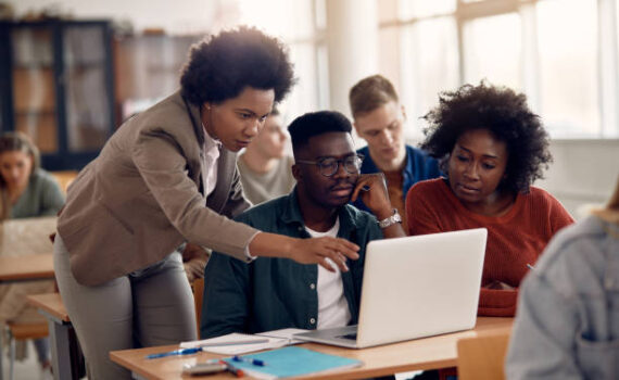 post-1 African American professor and her students using laptop during lecture in the classroom.