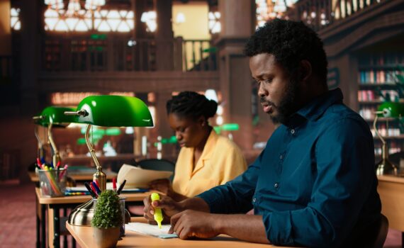 Black university student highlighting relevant phrases to learn the summary of the class lesson, memorizing key information by underlining important terms. Academic library. Camera A.